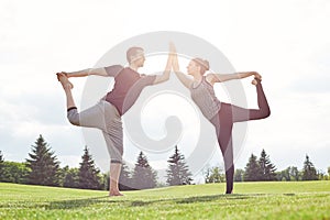 In harmony with nature. Young couple stretching and doing yoga exercises in open field on a sunny morning. Acro yoga