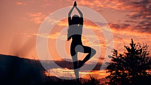 In harmony with oneself and the world. Silhouette of woman standing at yoga pose during an amazing sunset.