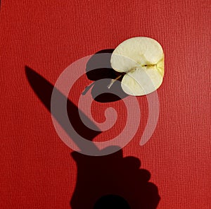 Harsh shadow of a hand holding knife above an apple cut in half