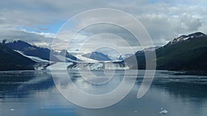 Harvard Glacier at the end of College Fjord Alaska. Wide glacier carving its path to the sea. Mountains peaks water and clouds