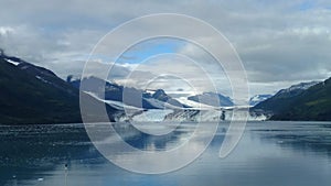 Harvard Glacier at the end of College Fjord Alaska. Wide glacier carving its path to the sea. Mountains peaks water and clouds