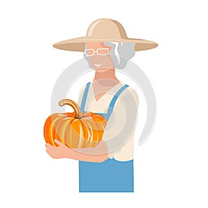 An elderly woman in work clothes and a sun hat harvests a pumpkin photo