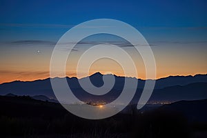 harvest moon rising behind silhouetted mountain range, with stars and clouds visible in the night sky