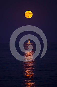 Harvest moon rising over a sailing boat