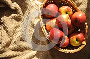 Harvest of red ripe apples in a straw basket. Washed fresh fruits on bedcover
