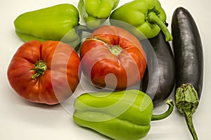 Harvest of vegetables, large red tomatoes, green sweet peppers and black and purple eggplants grown in Armenia lie on a white back