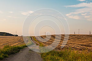 Harvested fields with cut straw and electivity power line columns in summer warm sunset evening light
