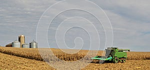 Harvester in corn field with grain bins