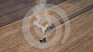 The harvester harvests the field and the last row remains. The tractor hauls a full flatbed. Aerial shot, camera goes up