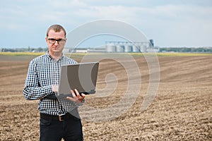 Harvesting concept. farmer in a field with a laptop on a background of a Agricultural Silos for storage and drying of grains,