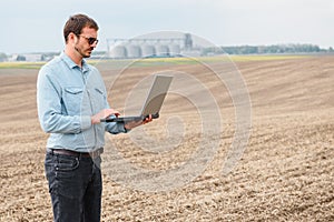 Harvesting concept. farmer in a field with a laptop on a background of a Agricultural Silos for storage and drying of grains,