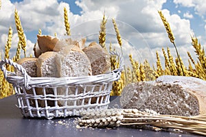 Harvesting crops concept. Fresh bread and wheat on table against golden wheat field and blue sky. Harvest season.