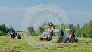 Harvesting hay. Tractor loading hay bales on a trailer.