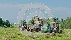 Harvesting hay. Tractor loading hay bales on a trailer.