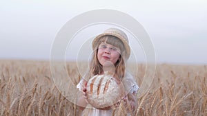 Harvesting, small fair kid girl bites tasty baked bread and smiles during outings in golden harvest grain wheat field