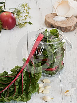 Harvesting vegetables. Chard leaf and cloves of garlic in the foreground. The jar is filled with chard leaves. Preparation for