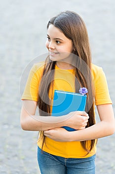 She has got the book she needs. Happy child hold book outdoors. Cute bookworm wear long hair in casual style. School