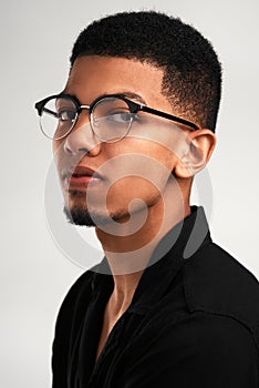 He has his eye on you. Portrait of a handsome young man wearing glasses while standing against a grey background inside