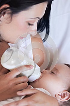 She has that mothers instinct. A mother feeding her baby boy a bottle of milk as he falls asleep.