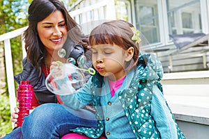 She has no trouble with bubbles. a mother watching her daughter blow bubbles outside.