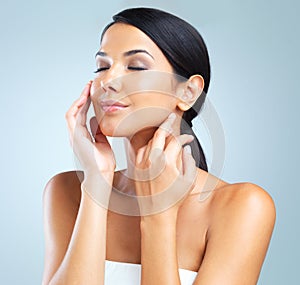 She has the perfect complexion. Cropped studio shot of a beautiful young woman touching her skin.