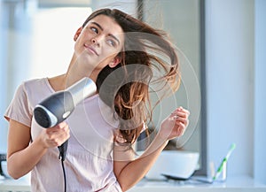 She has the perfect haircare routine. a beautiful young woman blowdrying her hair in the bathroom at home.