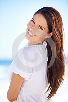 She has a sunny disposition. Cropped portrait of a beautiful young woman looking over her shoulder at the beach.