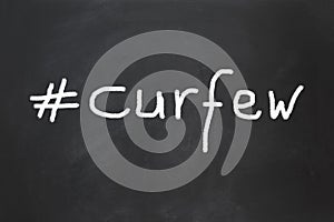 Hashtag curfew as handwritten text on chalkboard