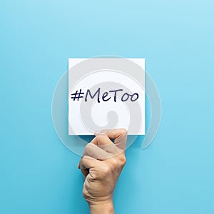 Hashtag  MeToo on white paper in hand isolated on blue background.  MeToo is a campaign for movement against sexual harassment