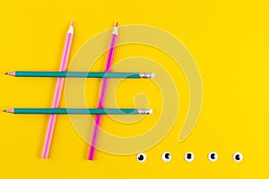 Hashtag sign from crossed colorful pencils on yellow background