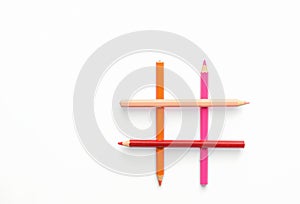 Hashtag sign from crossed colorful pink orange red peachy pencils on white background. Arts creativity social media networking