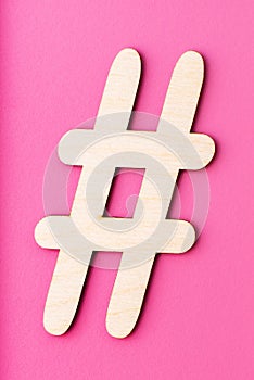 Hashtag sign made of wooden material on pink background