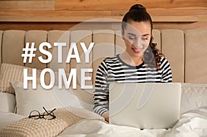 Hashtag Stayhome - protective measure during coronavirus pandemic. Young woman working on laptop in bed