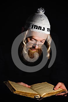 Hasidic jew reading Torah. Religious orthodox jew with sidelocks and red beard in white bale praying in the dark