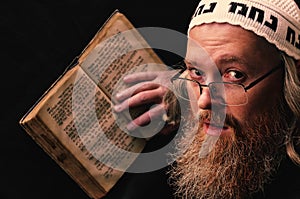 A Hasidic Jew reads Siddur. Religious orthodox Jew with a red beard and with pace in a white bale praying. Closeup