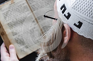 A Hasidic Jew reads Siddur. Religious orthodox Jew with a red beard and with pace in a white bale praying. Closeup