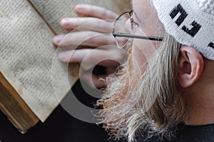A Hasidic Jew reads Siddur. Religious orthodox Jew with a red beard and with pace in a white bale praying. Closeup