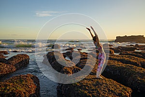 Hasta Uttanasana. Deflection back. Caucasian woman standing on big stone. Low tide. Yoga practice at the beach. Sunset time. Yoga