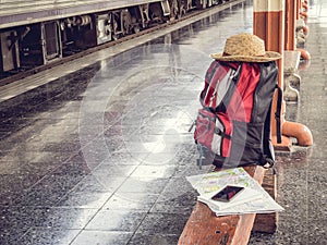 Hat, backpack, map, cellphone and notebook on bench at train station.