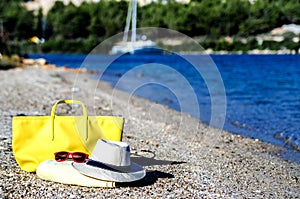 A hat, a beach bag, glasses and a towel lie on the beach amidst a beautiful coastline.