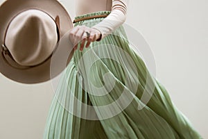 Hat, beige blouse and turqoise pleats skirt on light street backgraund.