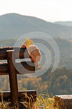 Hat with bouquet of wild flowers on wooden rustic bench in mountains forest valley. Travel, vacation, simple rural life