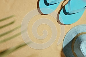 Hat and flip flops on beach sand, top view