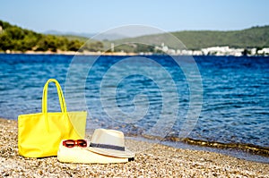 A hat, glasses, a bag and a beach towel on the sand by the sea.