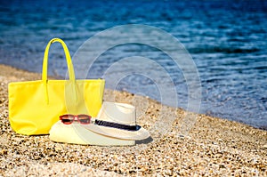 Hat, glasses, yellow beach bag and beach towel on the sand by the sea.