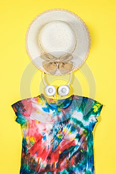 Hat, headphones and tie dye t-shirt on a yellow background. Flat lay.