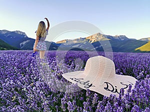 A hat in a lavender field with a young woman with her arms raised against the backdrop of the mountains