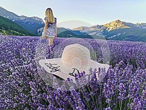 A hat in a lavender field with a young woman with her arms raised against the backdrop of the mountains