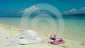 Hat and sandals on a sandy beach. White sandy beach and blue sea.