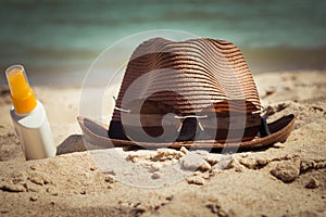 A hat with sunglasses and a bottle of sunscreen lotion